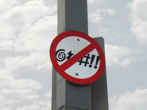 A no symbol sign featuring a spiral and text resembling "noise" with a red circle and slash, mounted on a pole.