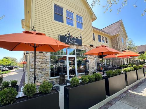 Exterior of Ella's restaurant featuring orange umbrellas, outdoor seating, and a stone facade on a sunny day.