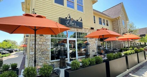 Exterior of Ella's restaurant featuring orange umbrellas, outdoor seating, and a stone facade on a sunny day.
