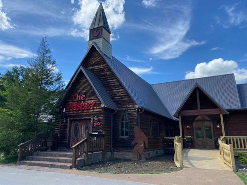 A rustic wooden building with a steeple, sign reading "The Abbey," and a Sasquatch silhouette near the entrance.