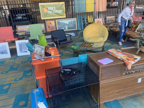 A vibrant outdoor display of mid-century furniture and decor, with colorful chairs, tables, and artwork for sale.