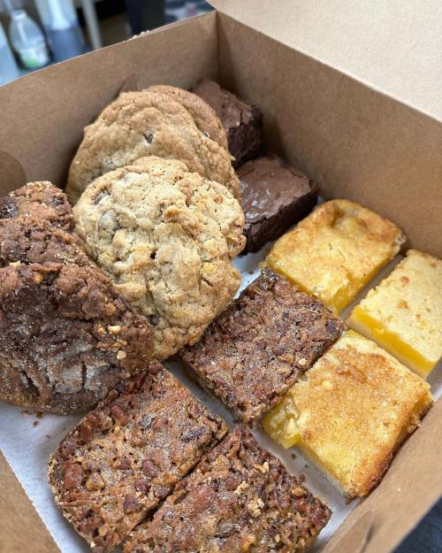 A box filled with assorted baked goods: cookies, brownies, and lemon bars arranged neatly.