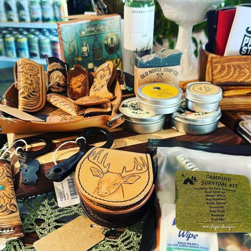 A display of handcrafted leather goods, candles, and a camping survival kit on a rustic table.