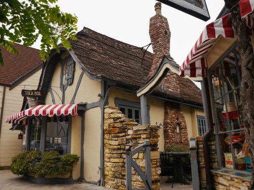 Charming cottage with a thatched roof, stone wall, and striped awnings, surrounded by greenery.