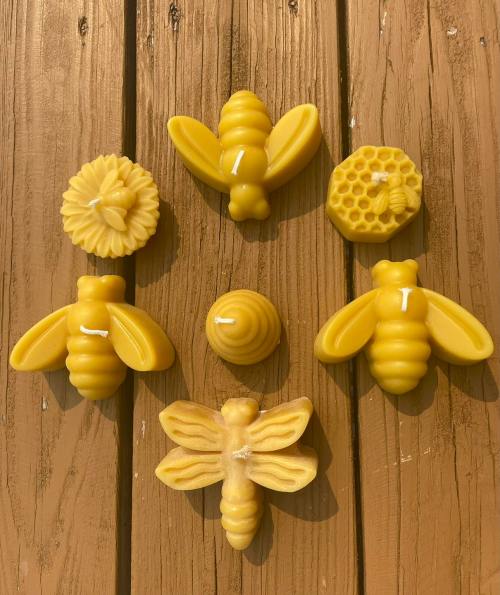 A collection of yellow beeswax candles shaped like bees, a flower, and a honeycomb, arranged on a wooden surface.