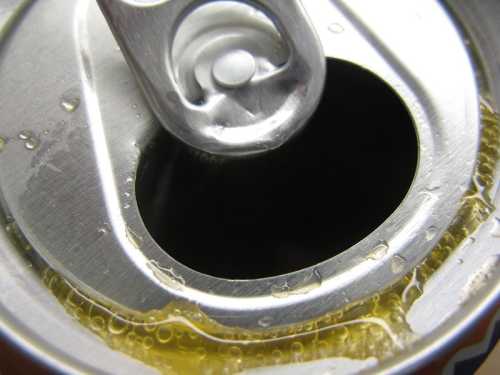 Close-up of an opened soda can, showing the pull tab and condensation around the rim.