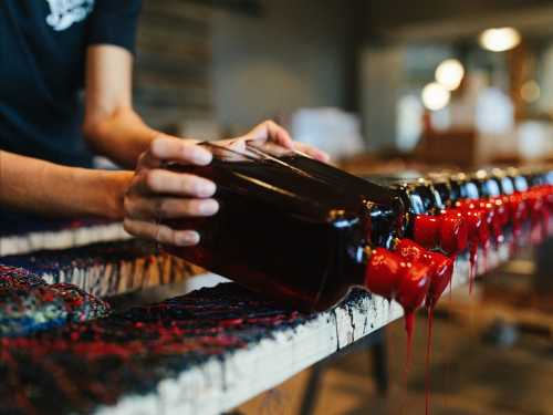 A person pours vibrant red dye from bottles onto a textured surface, creating a colorful, dripping effect.