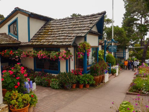 Charming building adorned with colorful flowers, surrounded by greenery and a pathway with people walking by.