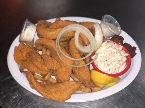 A plate of fried fish fillets with fries, coleslaw, onion rings, and lemon wedges, served with dipping sauces.