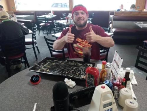 A man gives two thumbs up at a table with an empty food tray, surrounded by condiments and a timer.
