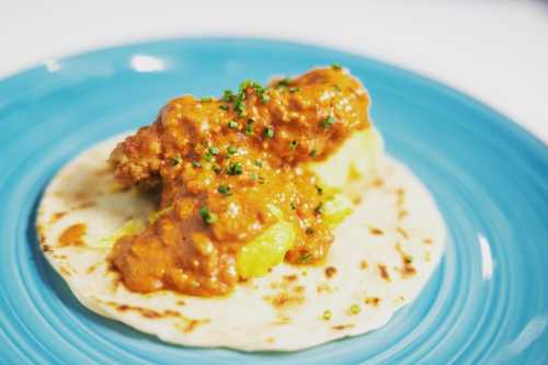 A soft tortilla topped with a savory sauce and garnished with green herbs, served on a blue plate.