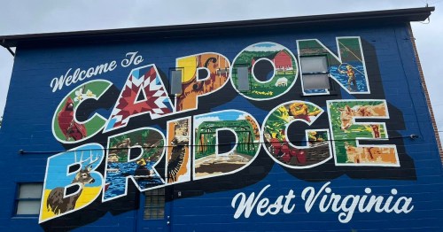Colorful mural welcoming visitors to Capon Bridge, West Virginia, featuring local imagery and vibrant lettering.