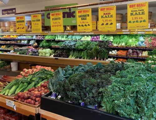 A vibrant display of fresh produce, including kale, plums, and various vegetables, with price signs in a grocery store.
