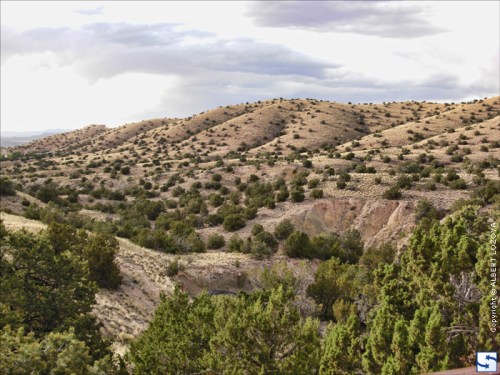 A scenic view of rolling hills covered with sparse vegetation under a cloudy sky.