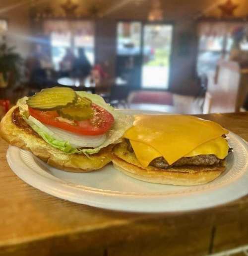 A close-up of a cheeseburger on a plate, featuring lettuce, tomato, pickles, and melted cheese on a toasted bun.
