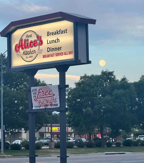 Sign for Aunt Alice's Kitchen advertising breakfast, lunch, and dinner, with a full moon visible in the background.