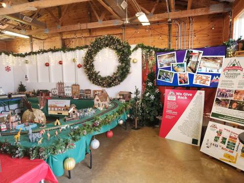 A festive display featuring a model train set, holiday decorations, and informational boards in a cozy indoor space.