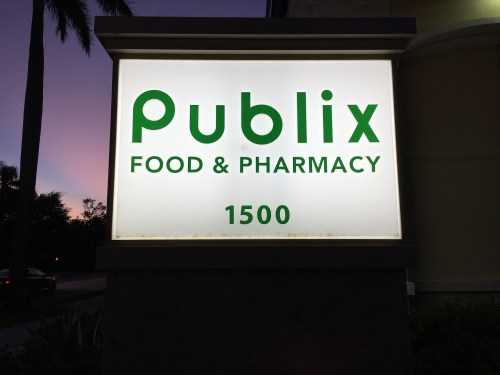 Sign for Publix Food & Pharmacy, displaying the name and address, illuminated against a twilight sky.