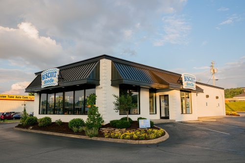 Exterior of a Biscuit Boodle restaurant with a modern design, surrounded by landscaping and a parking lot.