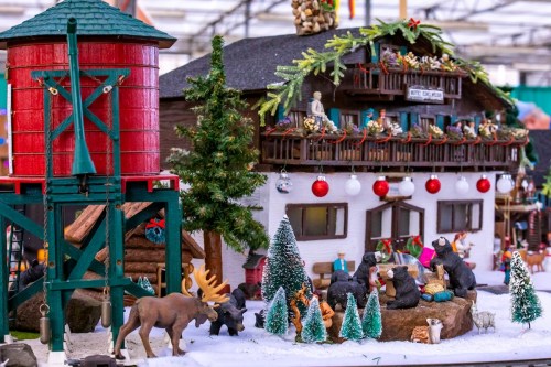 A festive miniature scene featuring a cabin, trees, animals, and holiday decorations in a snowy setting.
