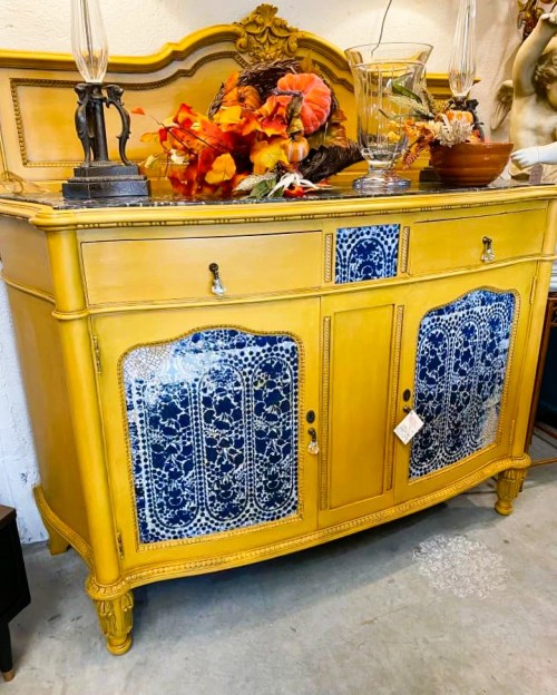 A vintage yellow sideboard with blue decorative panels, topped with autumn decor and lamps.