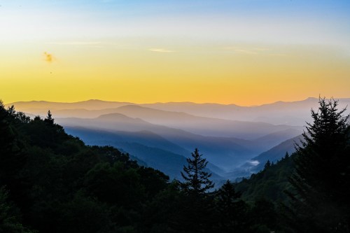 A serene mountain landscape at sunset, with layered hills and a gradient sky transitioning from orange to blue.