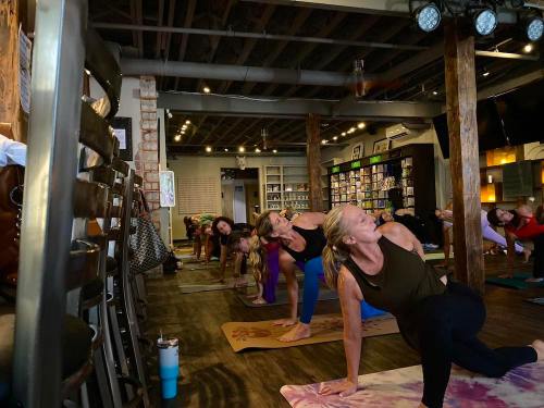 A group of people practicing yoga in a studio with wooden beams and shelves in the background.