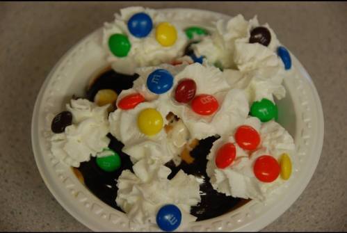 A bowl of ice cream topped with whipped cream and colorful candy-coated chocolates.