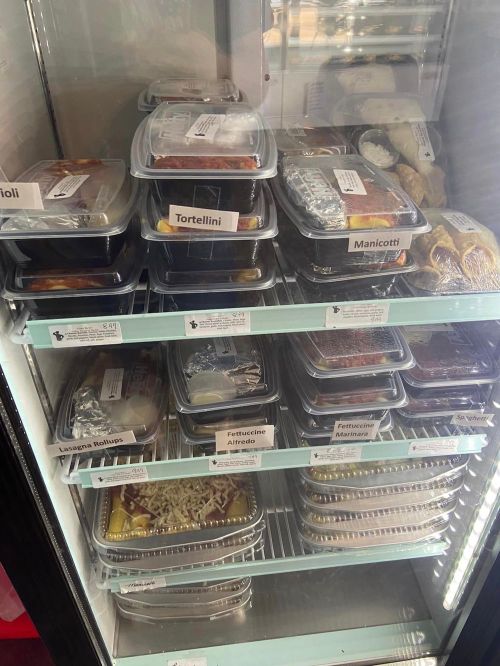 A refrigerator filled with labeled containers of various pasta dishes, including lasagna, tortellini, and manicotti.