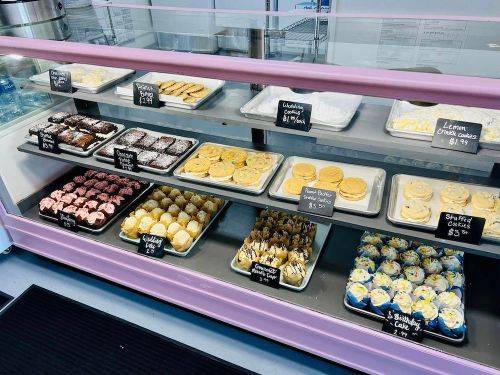 A display case filled with various baked goods, including cookies, brownies, and cupcakes, all labeled with prices.