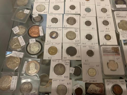 A display case filled with various coins, each labeled with prices and details, including silver and rare coins.
