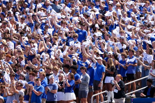 A large crowd of fans in blue and white clothing wave towels in a stadium, showing excitement and support.