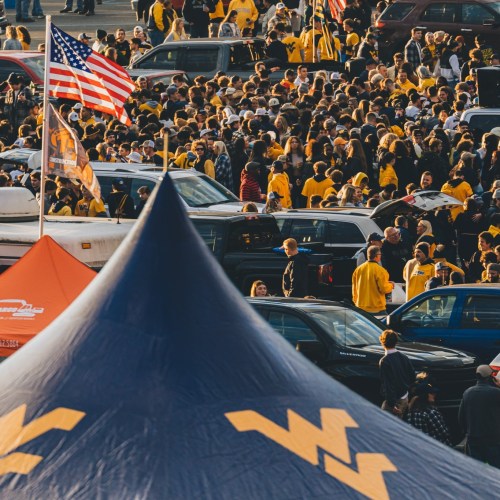 A large crowd of people in yellow shirts gathers in a parking lot, with an American flag and tents visible.
