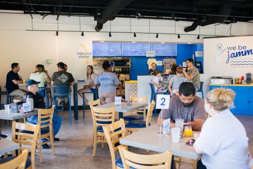 A busy restaurant interior with patrons seated at tables and a counter, featuring a bright blue and white decor.