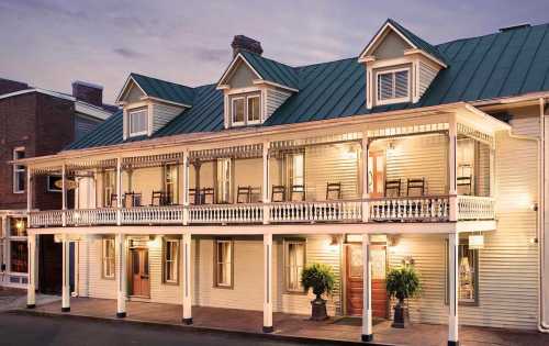 Historic building with a porch, rocking chairs, and warm lighting, set against a twilight sky.