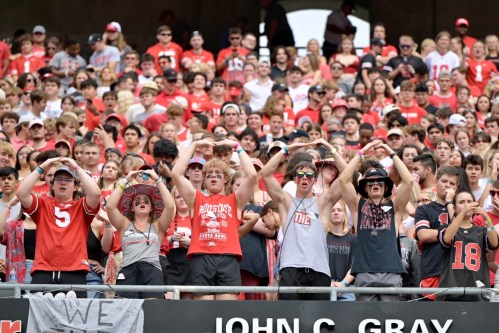A crowd of enthusiastic fans in red and gray clothing, cheering and making hand gestures at a sports event.