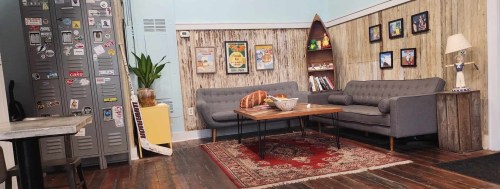 Cozy living room with gray sofas, a wooden coffee table, plants, and vintage decor on the walls.