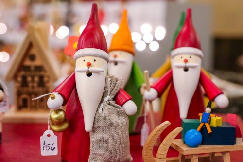 Colorful wooden Christmas figurines of gnomes with hats, holding a sack and bell, surrounded by festive decorations.
