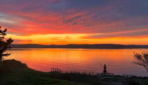 A vibrant sunset over a calm lake, with colorful clouds reflecting on the water and silhouettes of trees in the foreground.