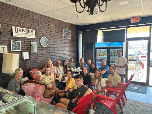A group of people sitting together in a cozy bakery, smiling and enjoying their time. Bright, inviting atmosphere.