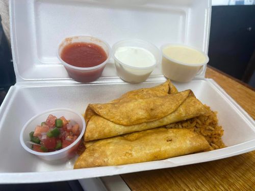 A takeout container with three crispy taquitos, rice, and three small cups of salsa, sour cream, and cheese sauce.