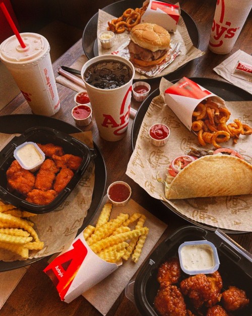 A table spread with fast food from Arby's, including curly fries, chicken nuggets, a sandwich, and drinks.