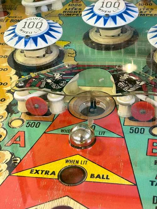 Close-up of a vintage pinball machine's playfield, featuring scoring areas and a shiny silver ball.