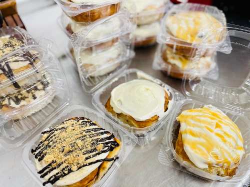 A variety of delicious cinnamon rolls in clear plastic containers, topped with icing and drizzles.
