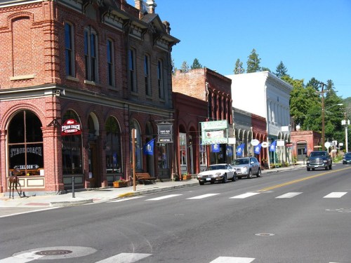 A charming street lined with historic brick buildings, shops, and parked cars under a clear blue sky.