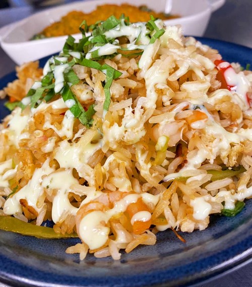 A close-up of a plate of fried rice topped with green herbs and drizzled with sauce, served with a side dish in the background.