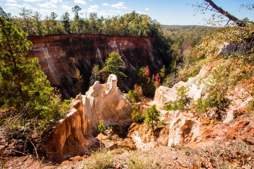 A scenic view of a deep canyon with steep, colorful cliffs and lush trees under a bright blue sky.