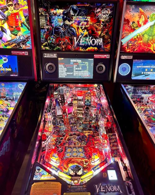 A vibrant pinball machine themed around Venom, featuring colorful artwork and illuminated playfield elements.