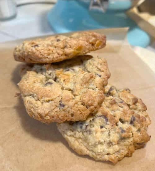 Three freshly baked cookies with chocolate chips and nuts, resting on a piece of parchment paper.
