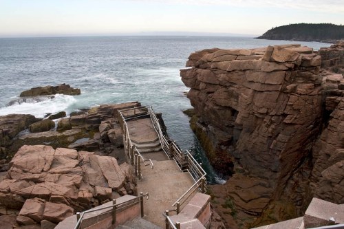 A rocky coastline with a pathway leading down to the water, surrounded by cliffs and gentle waves.